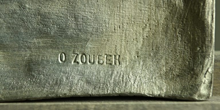 Velký polychromovaný cínový reliéf Ifigenie vytvořil Olbram Zoubek v dubnu roku 1985. Vznikl jako výřez z původního cementového reliéfu stejného jména, který měl rozměr  62 x 62 cm.