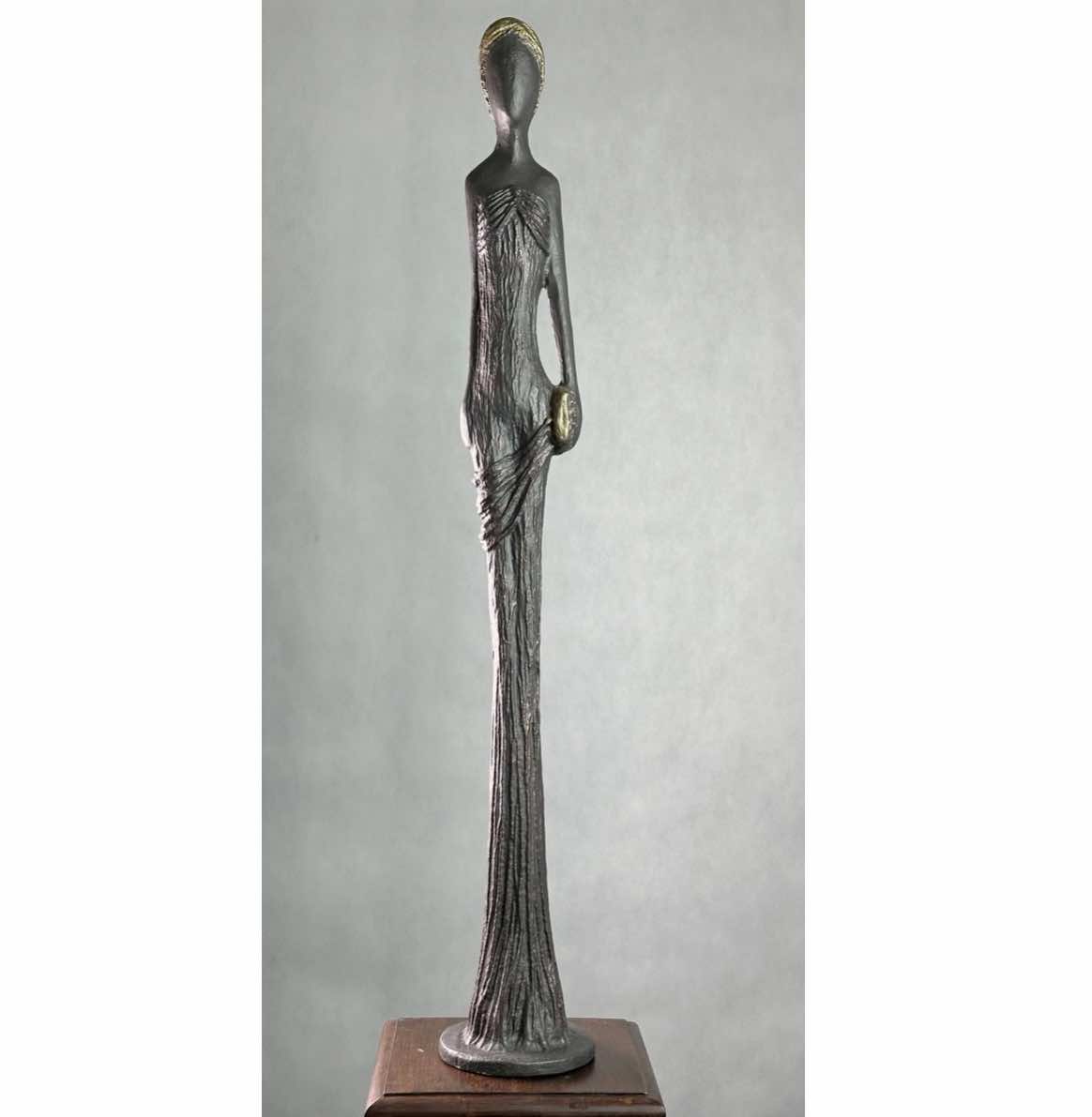 Socha Dívka 105 s kabelkou, měděná, zlaté vlasy znázorňuje velmi štíhlá, 105 cm vysoká postava ženy, dívky, jejíž šat tvoří zároveň podstavec sochy, což působí velmi ladně a celistvě.